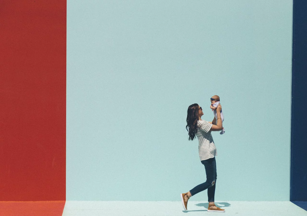 A parent lifting their baby into the air against a bright wall